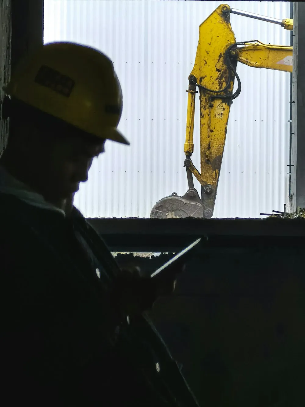 Field worker silhouetted beside an excavator on site