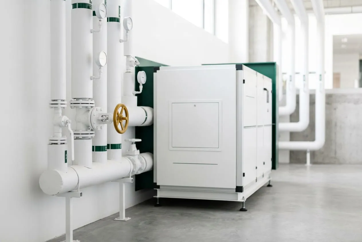 Empty white plant room with neatly run pipework and a single gold valve wheel