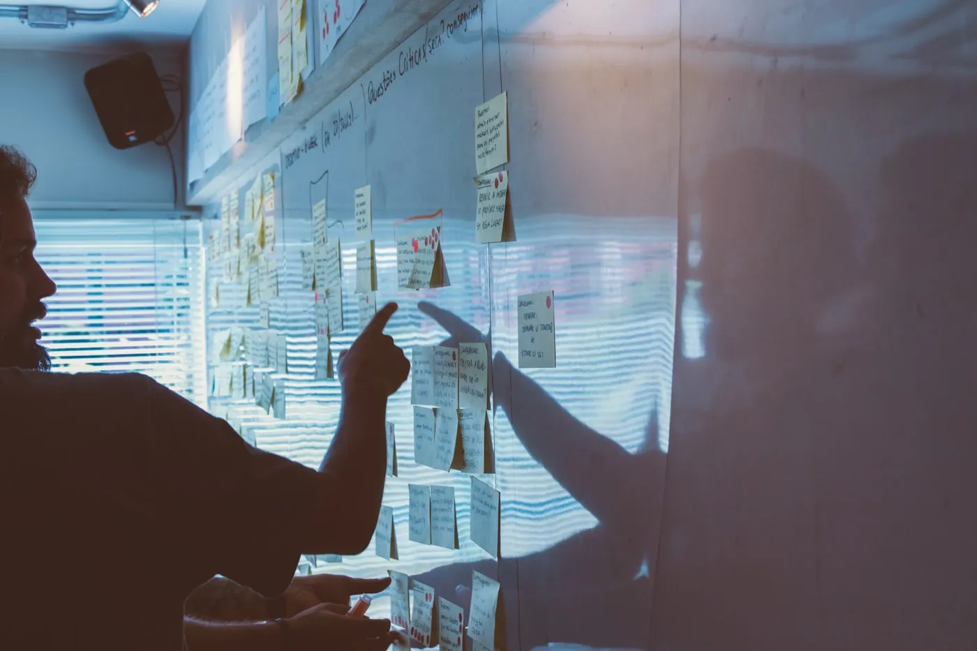 Two people mapping dependencies on a glass wall covered in diagrams