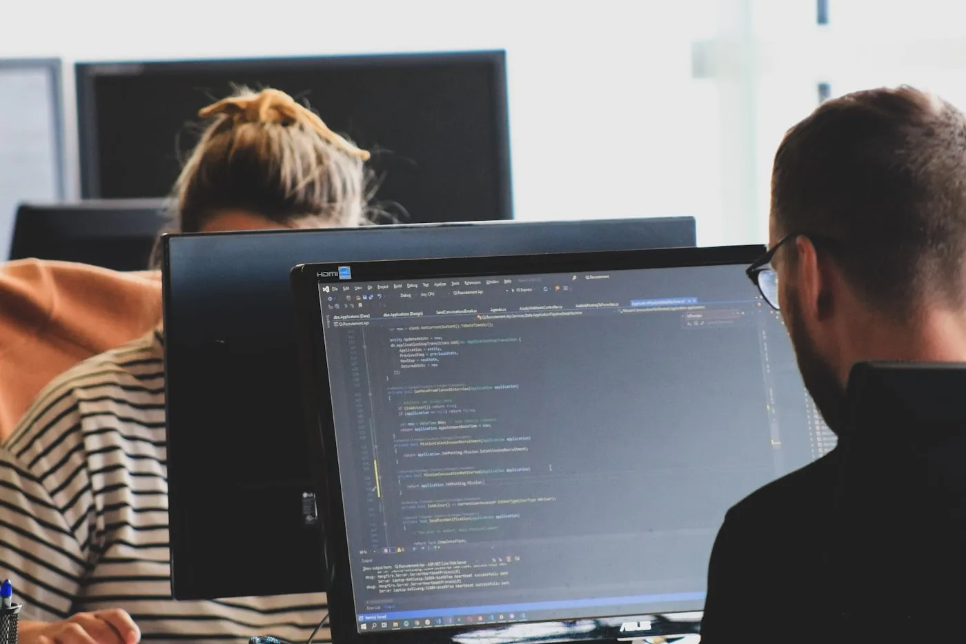 Two developers working at monitors showing code