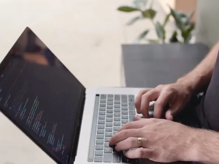 Hands typing on a laptop showing an editor full of code
